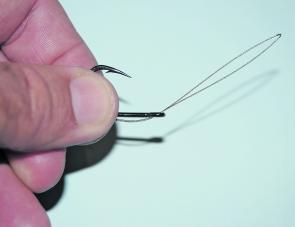 Cut a piece of wire between 16-18cm long and fold in half, pinching the mid-way spot so that there is a small, prominent crease. Pass this section through the eye of the hook so that the tag ends face away from the gape as shown. Hold the hook and the tag